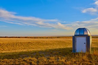 Pequena estação meteorológica instalada em uma extensa pastagem sob céu azul.