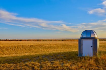 Pequena estação meteorológica instalada em uma extensa pastagem sob céu azul.