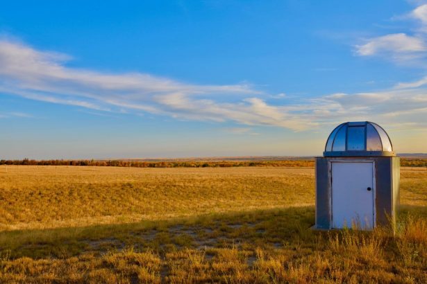 Pequena estação meteorológica instalada em uma extensa pastagem sob céu azul.